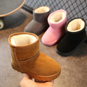 Chausson botte marron fourrée, tenue dans une main, dans l'arrière plan , le même modèle gris , rose, et noir posé au sol près d'un skateboard