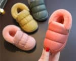 Plusieurs chaussons rembourrés pour bébé , trois chaussons unique pour chaque couleur , rose, jaune, et gris et une autre rose est tenue par une main de femme.