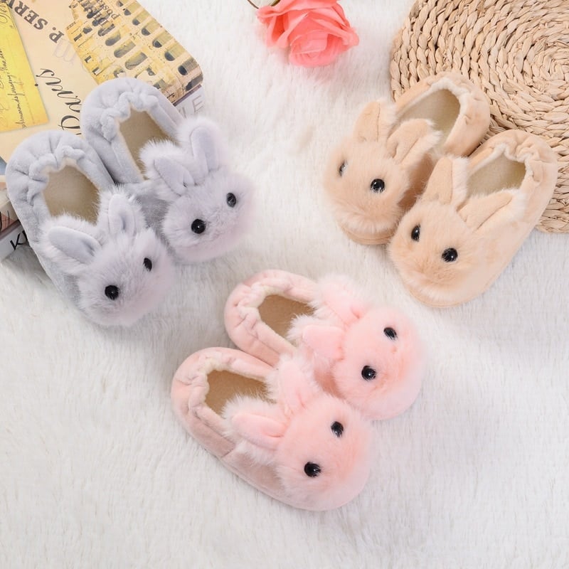 trois paires du même modèle de chaussons en forme de petits lapins, l'une est rose, l'autre grise et la dernière beige, ils sont disposés par paires sur le sol