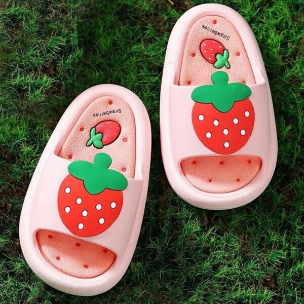 petit chaussons d'été pour bébé rose et ouverts avec une fraise rouge dessinée sur le dessus , et ils sont posés sur de l'herbe verte