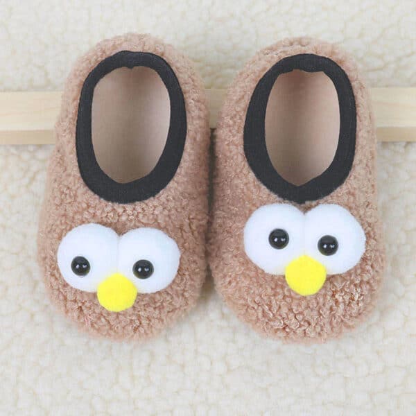 pantouffles chaussettes pour enfants avec des petits yeux de hibou , ils sont beige et posé au sol