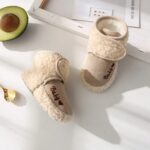 Chaussettes Chausson Garçon Style Botte en Fourrure et Coton posée sur une table blanche avec un cadre blanc et un avocat